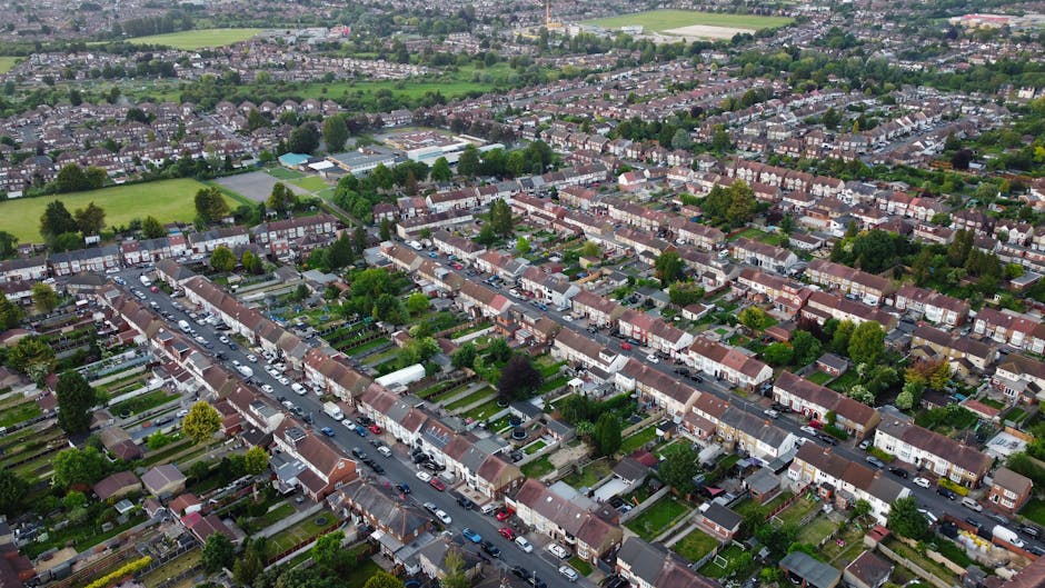An aerial view of a densely populated residential neighbourhood featuring a grid-like pattern of streets lined with terraced houses, each with small back gardens and pitched roofs. The foreground show