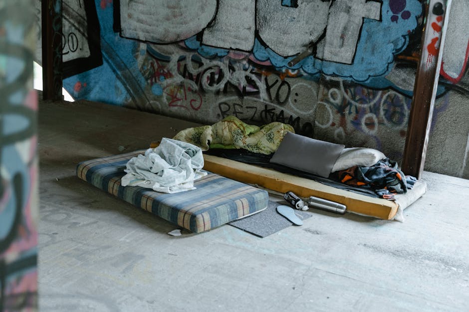 A bedroom interior featuring a large, plush off-white mattress resting on a matching bed frame with a padded headboard. The mattress has a textured surface with visible tufting and a manufacturer's la